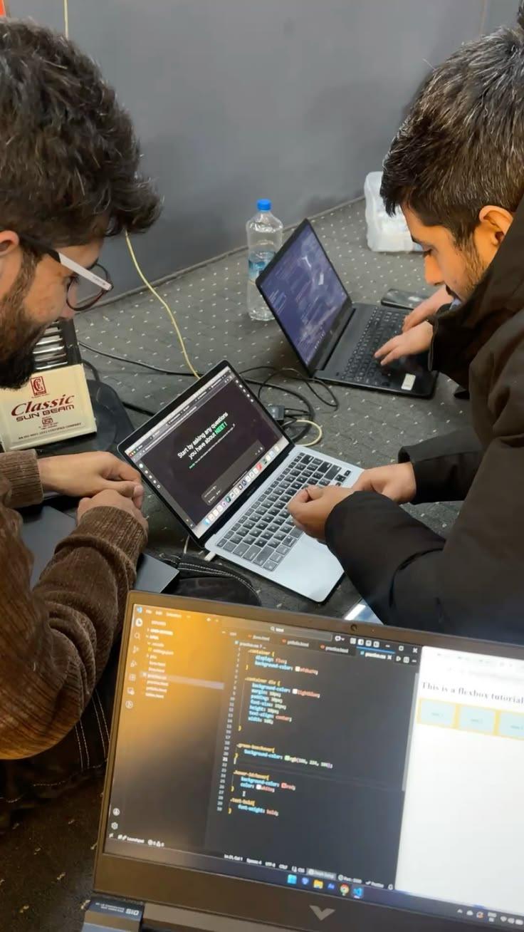 Two people working through code together on laptops at a small bootcamp table