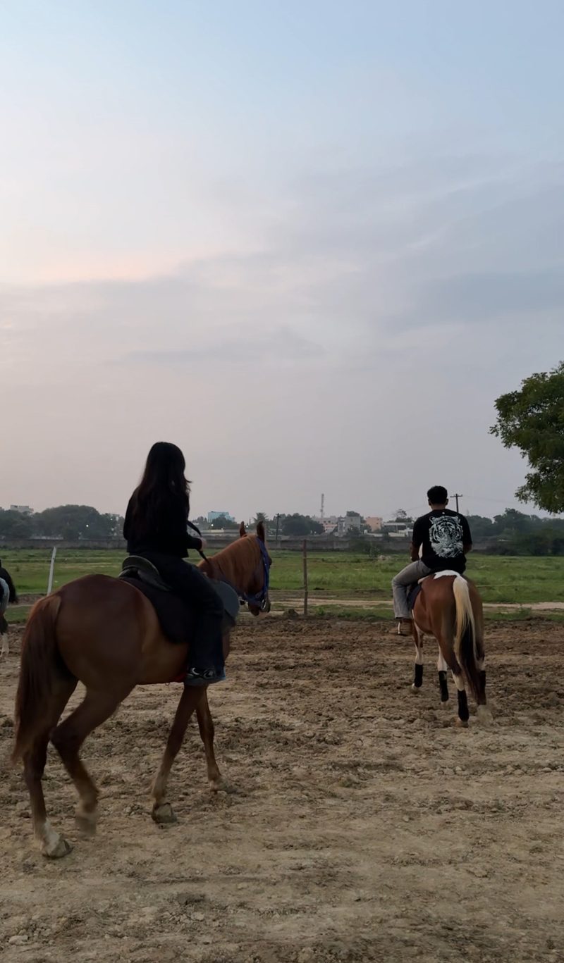 Two riders on horseback crossing an open ground at dusk, town rooftops behind