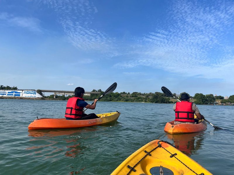 Two kayakers paddling across an open lake under a bright sky